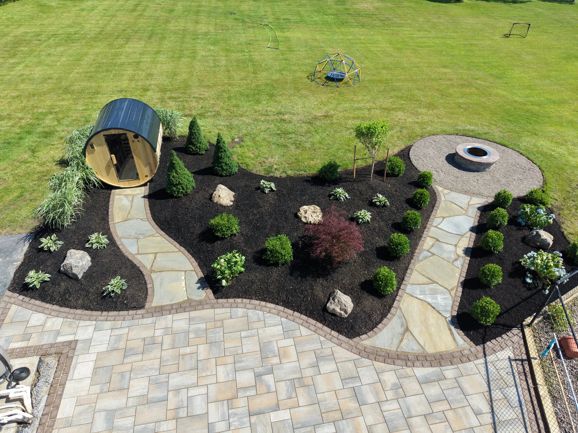 Overhead view of curved paths, a barrel sauna, and new planting around a paver patio