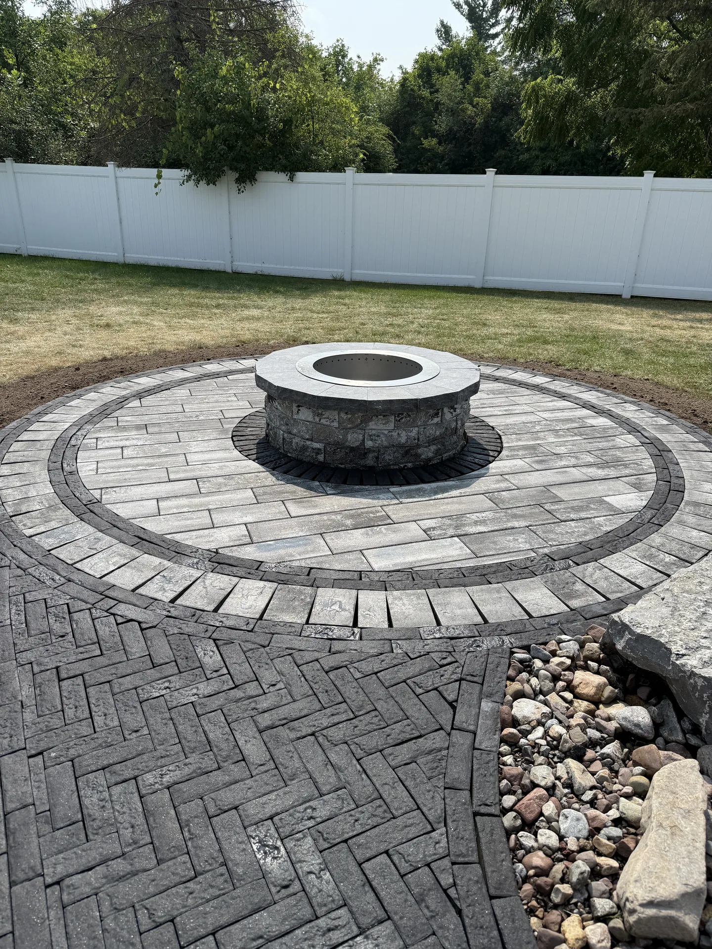 Circular paver terrace with a stone fire pit and dark border