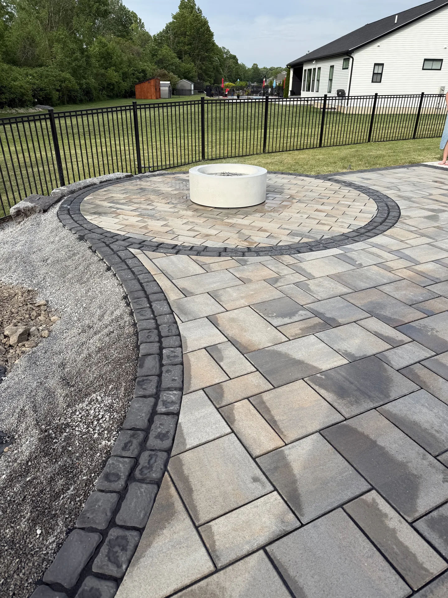 Paver patio with a circular inset and curved dark border beside a lawn