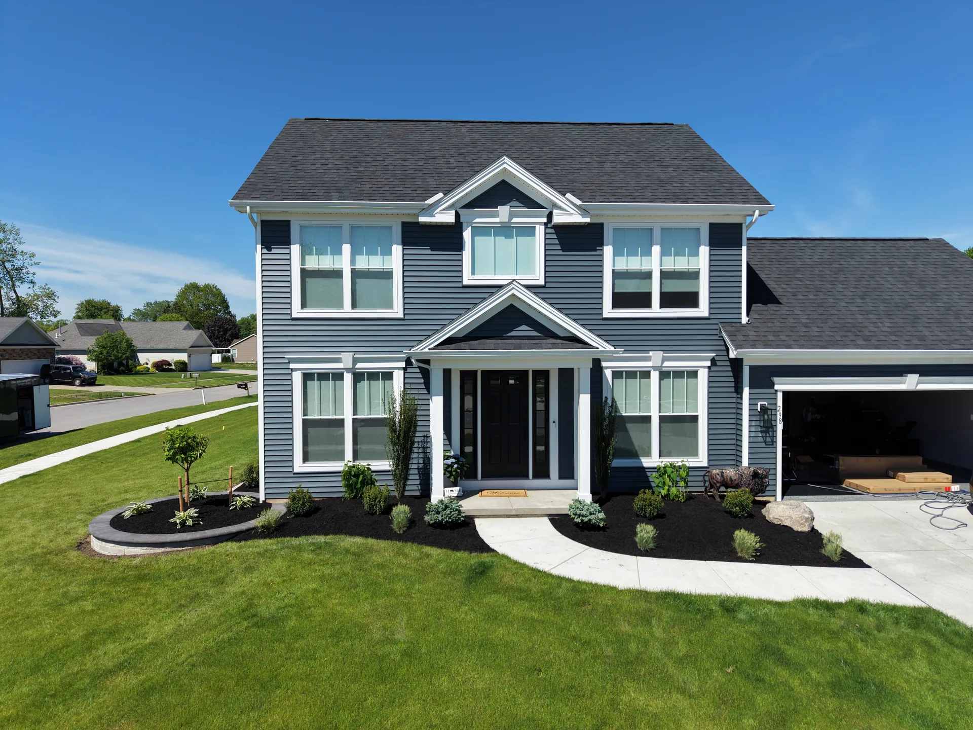 Front lawn and dark mulched planting beds with shrubs and ornamental trees beside a gray home