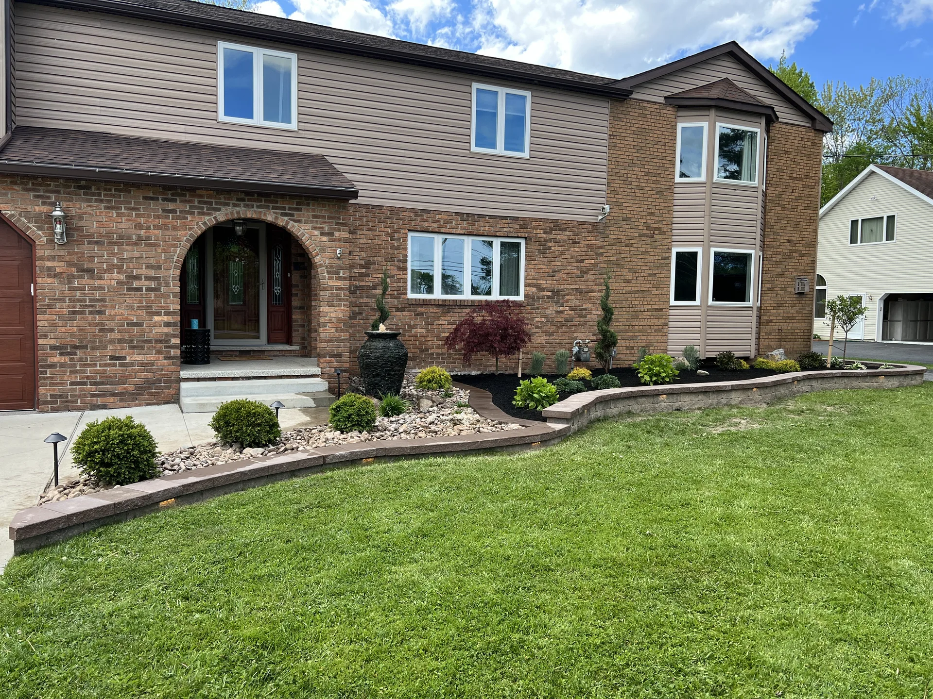 Shrubs and stone-edged planting beds along the front of a brick home