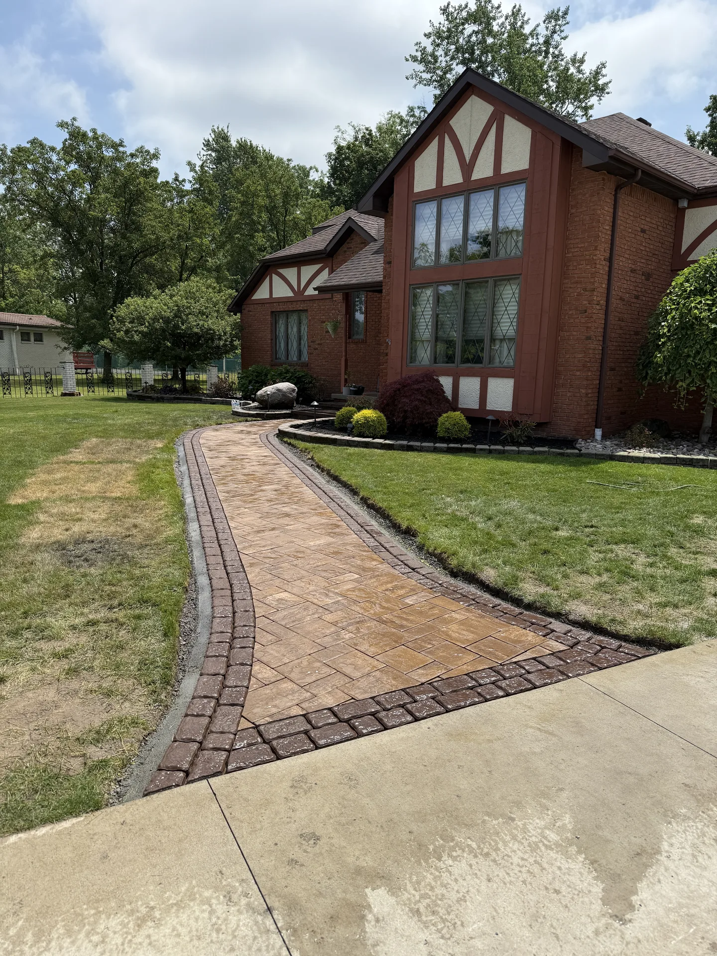 Curving paver walkway leading from the sidewalk to a brick home