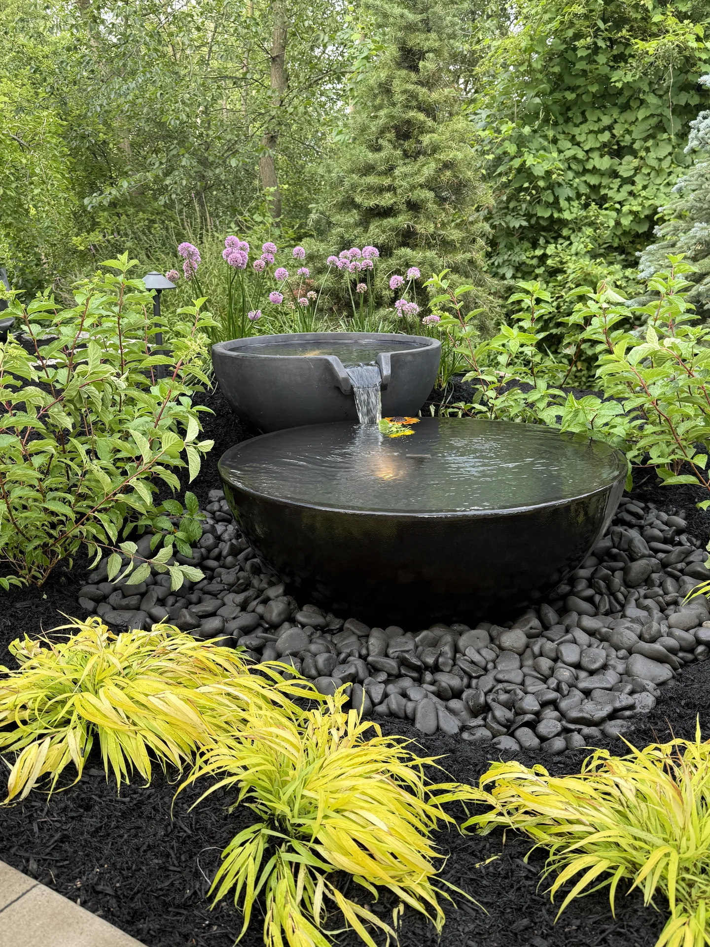 Two-tier bowl fountain set among ferns and leafy garden plants