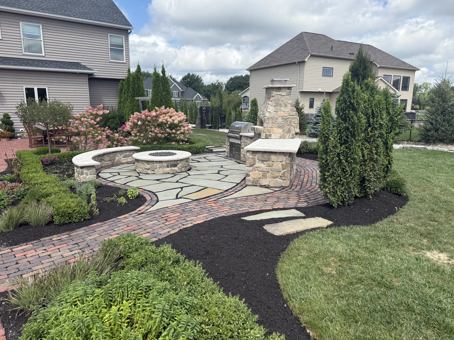 Layered shrubs and dark mulch around a stone outdoor kitchen and patio