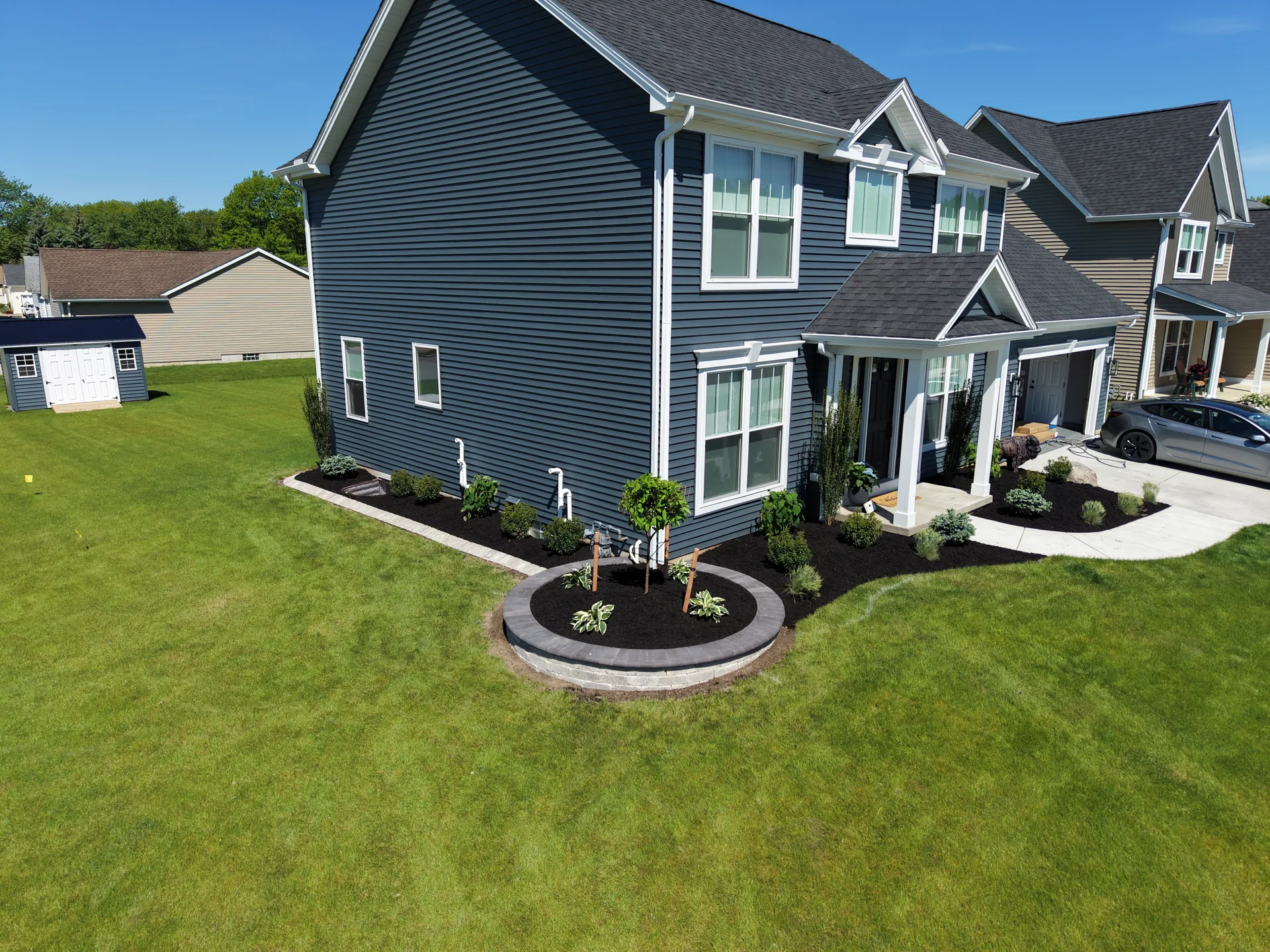 Lawn, curved planting beds, and shrubs around a gray two-story home