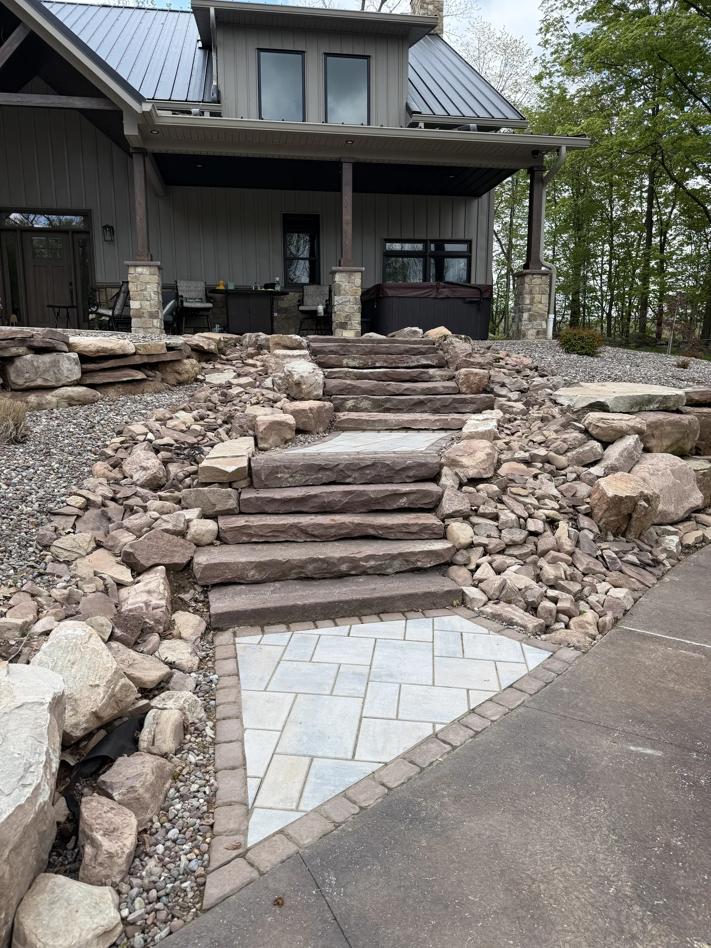 Broad natural stone steps connecting a lower paver path to a covered patio