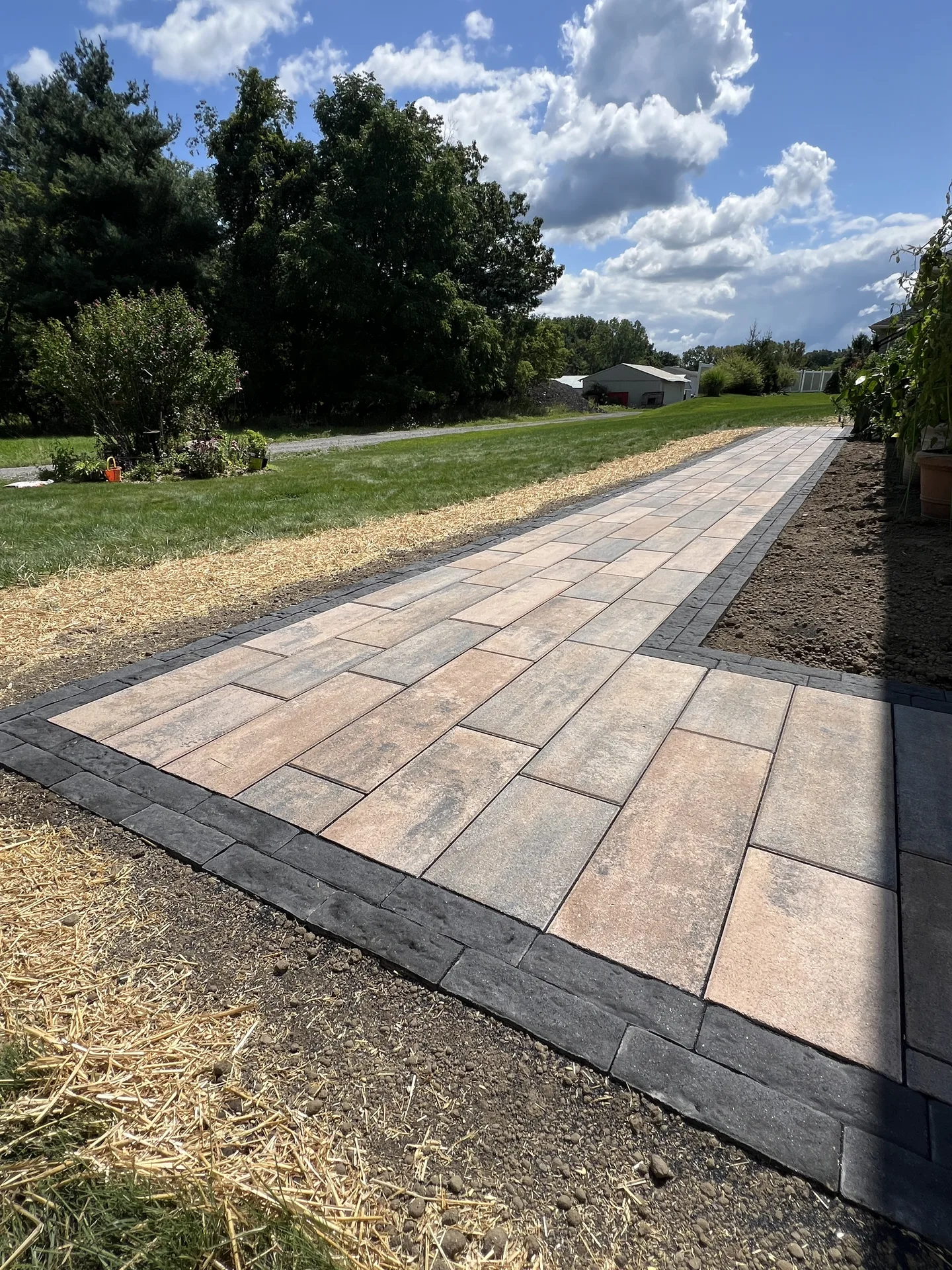 Long paver walkway with a contrasting dark border alongside a lawn