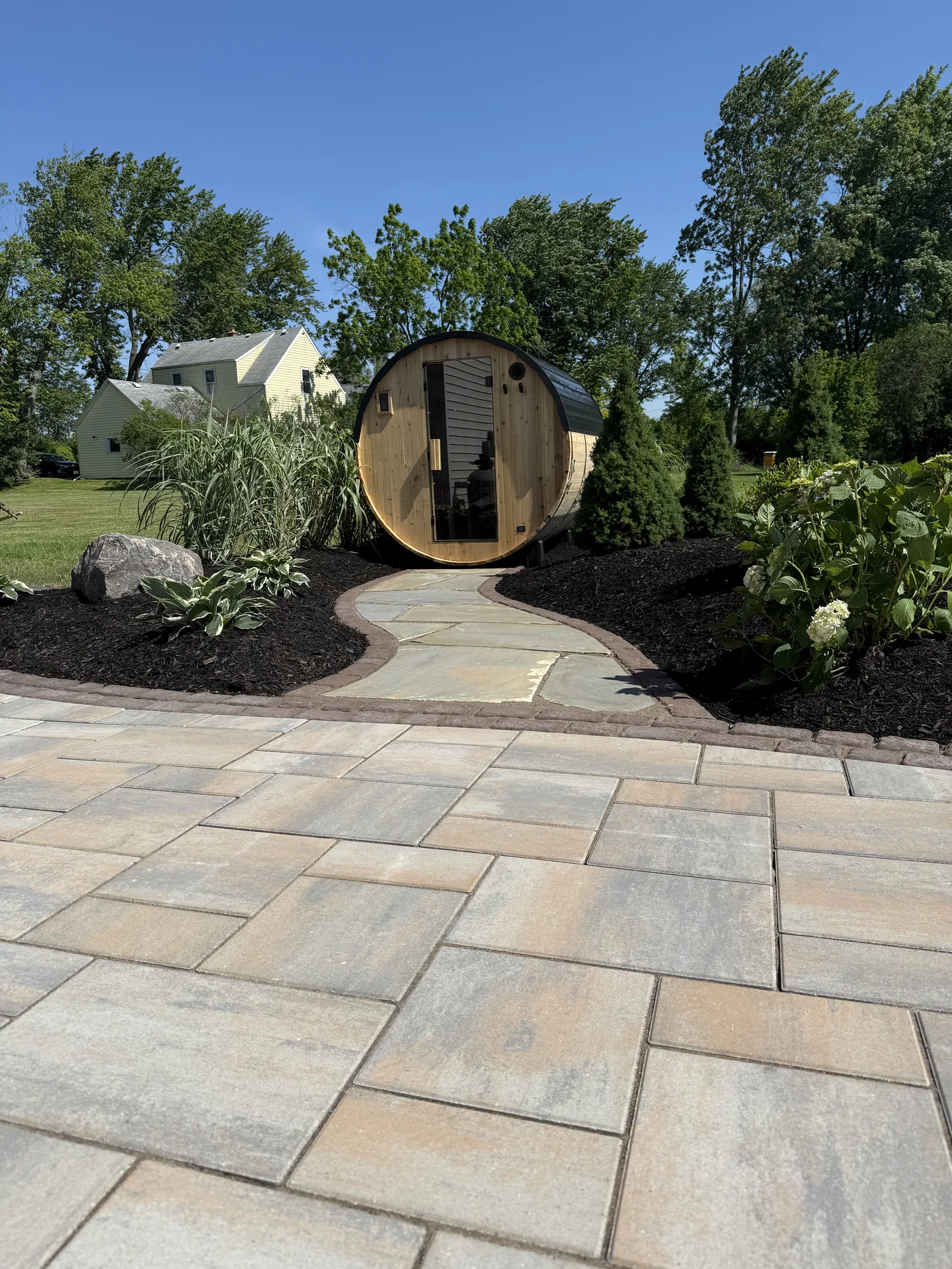 Curved garden path leading from a paver patio to a barrel sauna