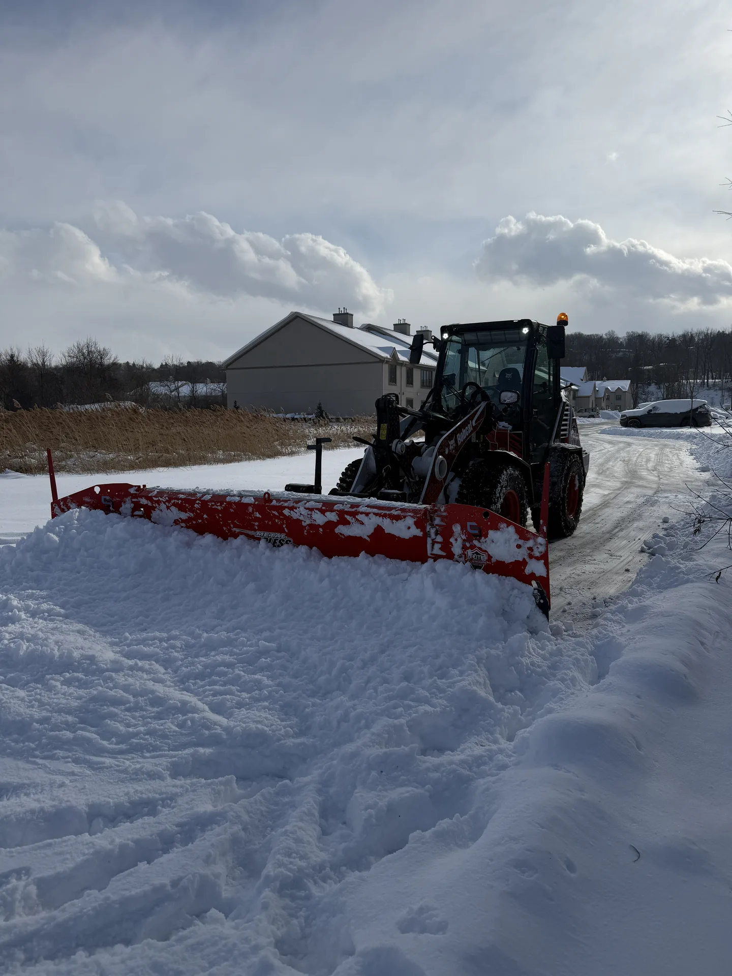 Tractor clearing deep snow with a wide red snowplow