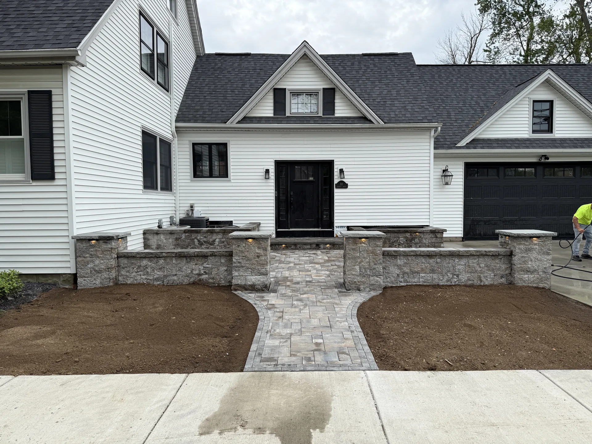 Stone entry courtyard with low walls and columns in front of a white house