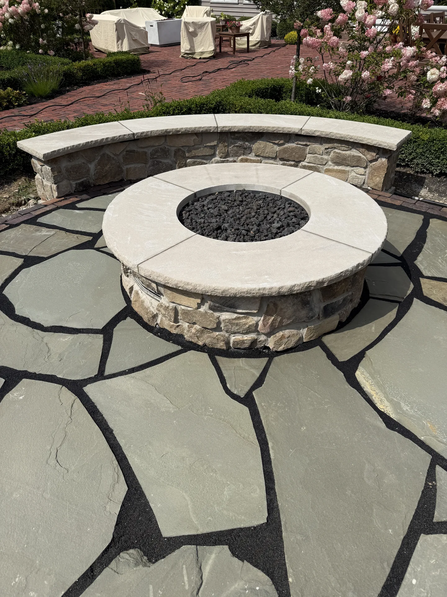 Circular stone fire pit and curved seating wall on a flagstone patio
