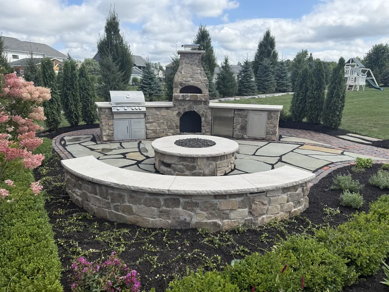 Stone outdoor kitchen and fire pit surrounded by planting