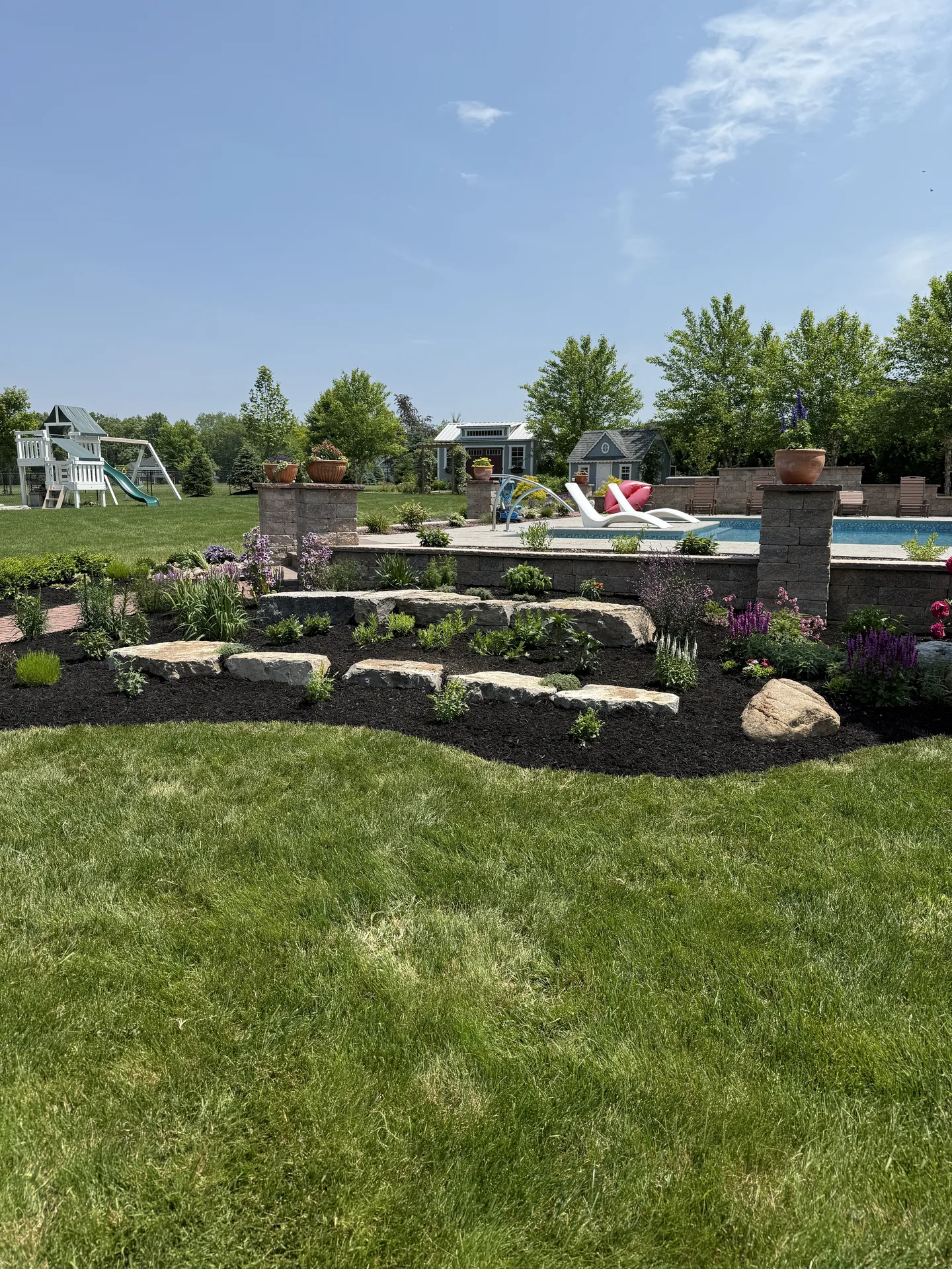 Tiered stone garden beds with shrubs and lawn beside a patio