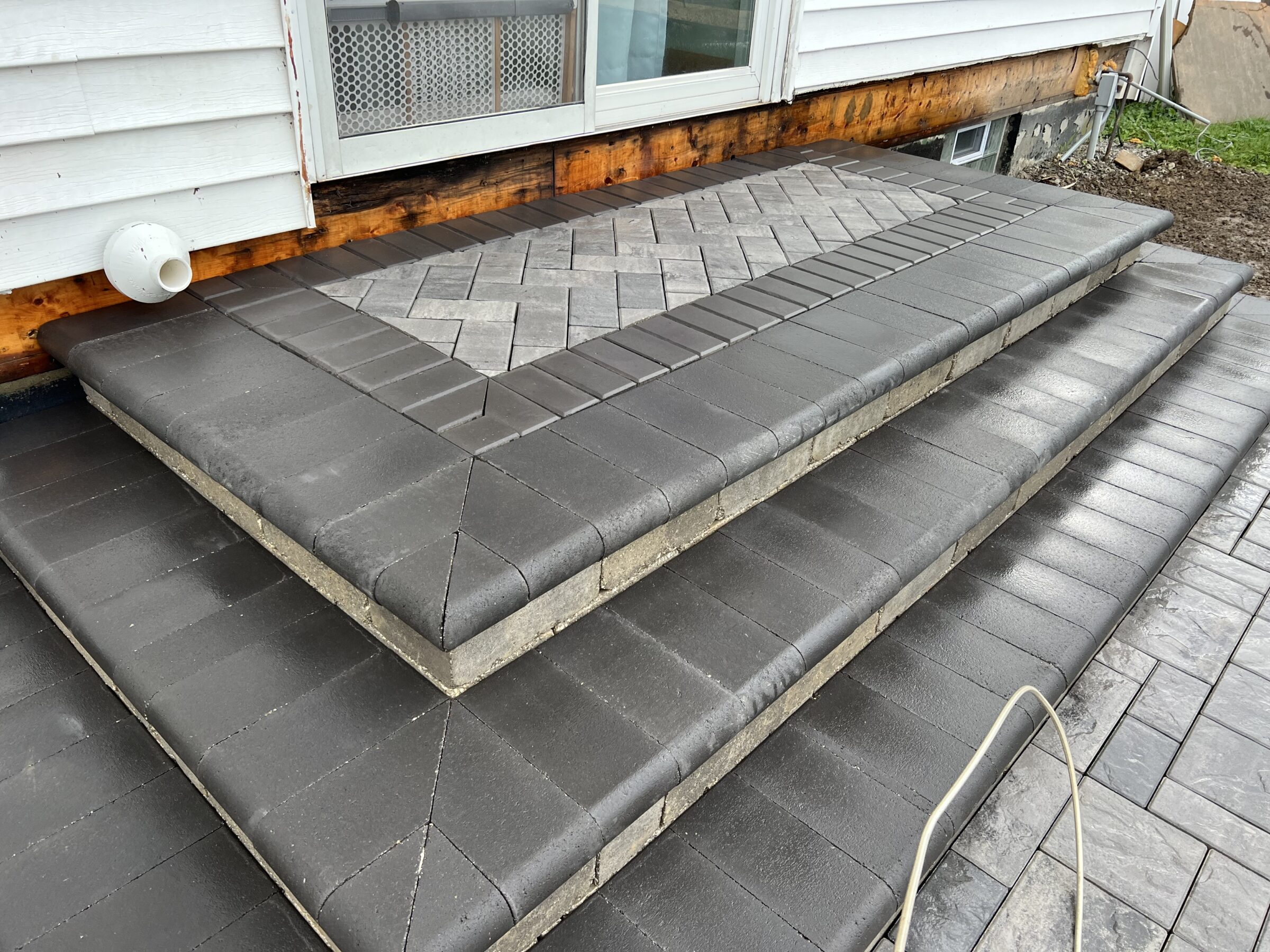 Concrete steps leading to a building with a wooden exterior, featuring a patterned tile design. Simple, modern construction.