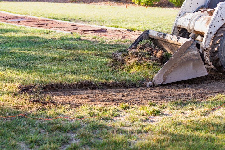 A small bulldozer removes a strip of grass on a sunny day, preparing the ground for landscaping or construction work.